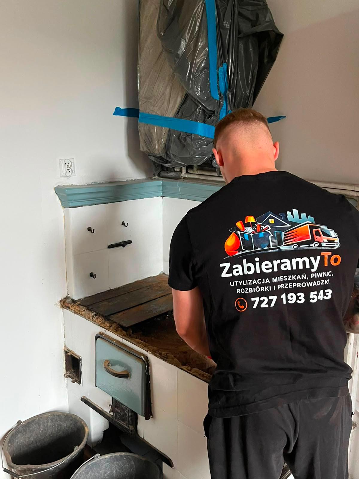 Pracownik ZabieramyTo w firmowej koszulce demontuje starą kuchnię węglową
