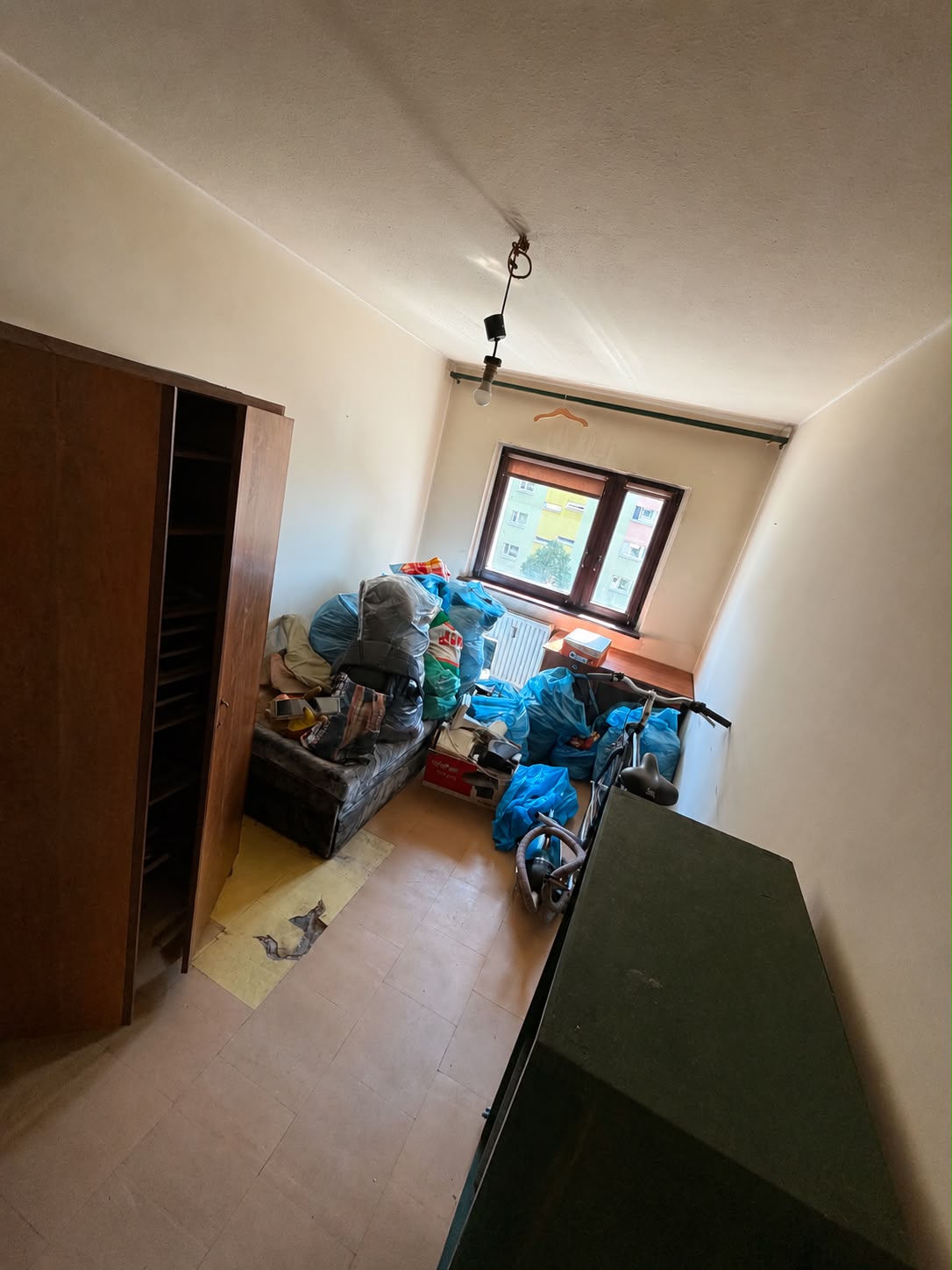 Mały pokój z zabudowaną szafą i rzeczami w workach przed wywozem